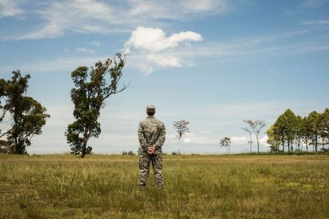 Solitary Soldier Standing Facing Horizon Clasping Hands in Camouflage Uniform on Grassland