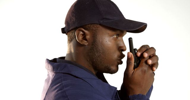 A young African American man is focused as he communicates through a walkie-talkie, with copy space. His attire and the device suggest he could be a professional in a field requiring coordination, like security or event management.