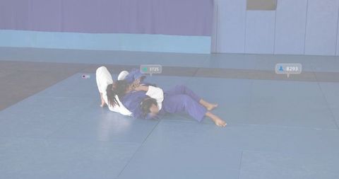 Teenage girls grappling in judo gis on blue tatami mats with digital counters