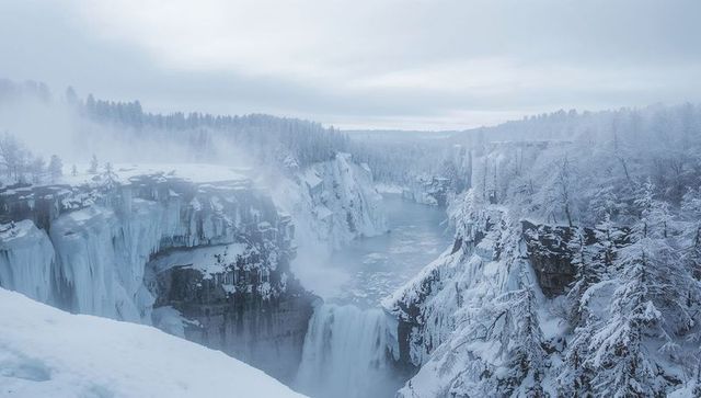 Frozen waterfall plunging through snow-covered canyon with misty icy cliffs