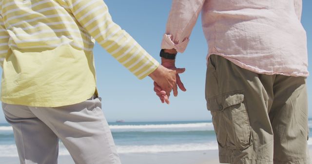 Mid section of senior caucasian couple holding hands on the beach. travel vacation retirement lifestyle