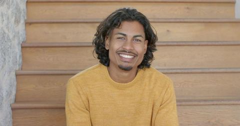 Smiling young man on wooden stairs in mustard sweater conveying warmth and approachability