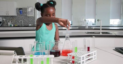 African girl pouring bright orange solution into flask during hands-on chemistry experiment