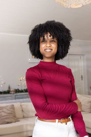 Confident african american woman smiling in cozy living room wearing burgundy top