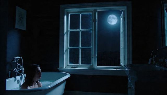 Moonlit bath scene featuring woman in clawfoot tub turning toward open window at night
