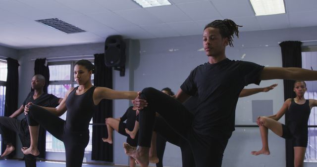 Diverse group of ballet dancers practicing balance in studio. Each person performing a similar pose, raising one leg and concentrating. Ideal for use in materials focused on dance education, teamwork, performing arts, flexibility, and fitness training.