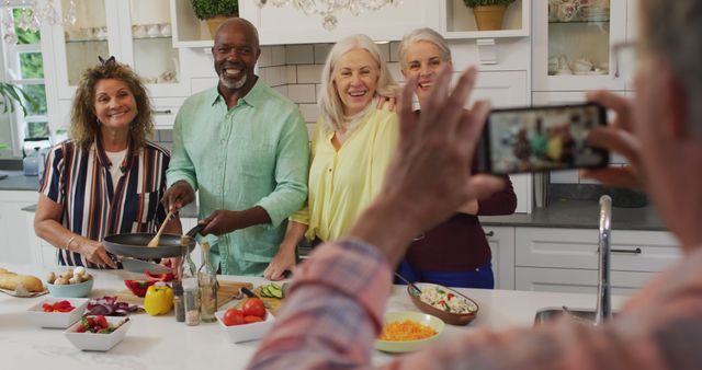 Image of happy diverse female and male senior friends preparing meal, taking photo. retirement lifestyle, spending quality time with friends and technology.