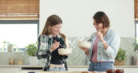 African american female friends tasting homemade meal at bright modern kitchen counter