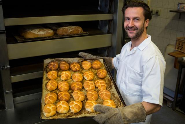 Portrait of smiling baker carrying a tray of baked buns