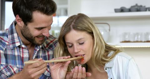 Young Couple Cooking and Tasting in Modern Kitchen