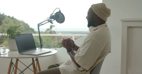 Remote podcaster recording from bright balcony studio with laptop, boom mic, headphones