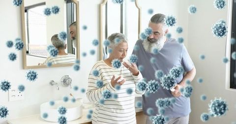 Elderly couple checking sore throat amid airborne virus particles at bathroom mirror