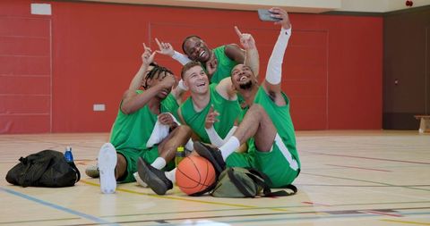 Green team basketball players taking selfie while resting on gym floor showing team spirit
