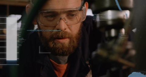 Bearded machinist inspecting spindle and chuck wearing safety goggles with hud overlay