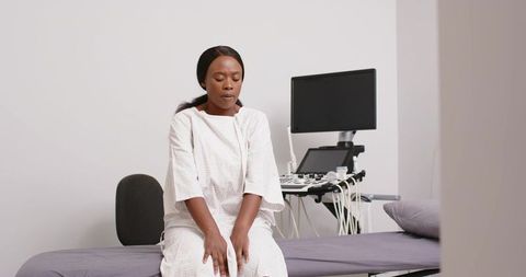 Female patient in medical gown sitting on examination table beside ultrasound machine