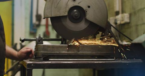 Cutting metal on abrasive chop saw producing sparks in industrial workshop
