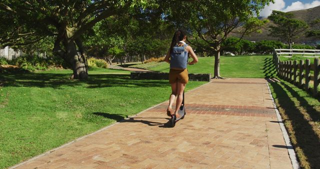 Woman Riding Scooter on Park Path with Green Trees and Blue Sky - Download Free Stock Images Pikwizard.com