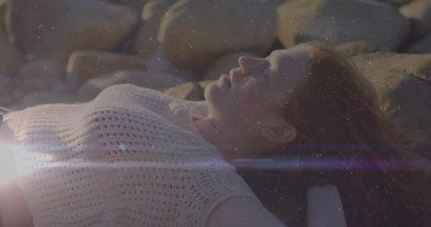 Woman relaxing on rocky shore with sunlit lens flare