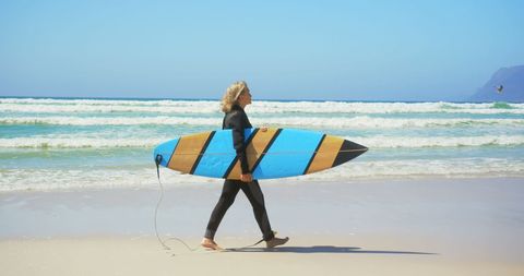 Elderly Female Surfer Carrying Surfboard at Beach Under Sunny Sky - Download Free Stock Images Pikwizard.com