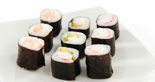 A plate of sushi rolls is presented against a white background, with copy space. Sushi, a traditional Japanese dish, consists of vinegared rice, seafood, and vegetables wrapped in seaweed.