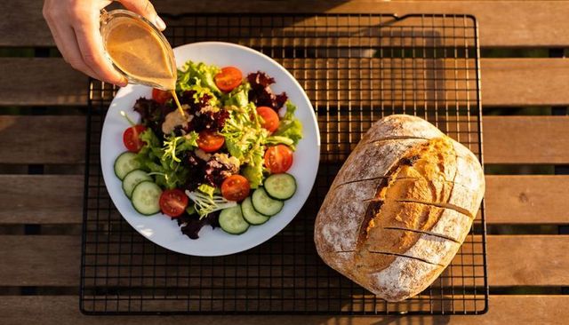 Pouring vinaigrette over fresh garden salad with crusty rustic bread on sunny patio table