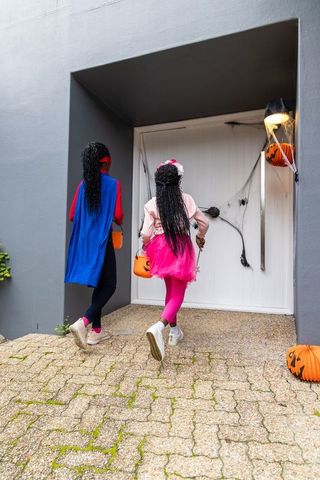 African american girls trick-or-treating at decorated front door with pumpkin buckets