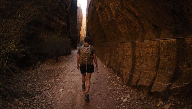 Solo hiker trekking narrow sandstone slot canyon with backpack, sunlight and rugged trail