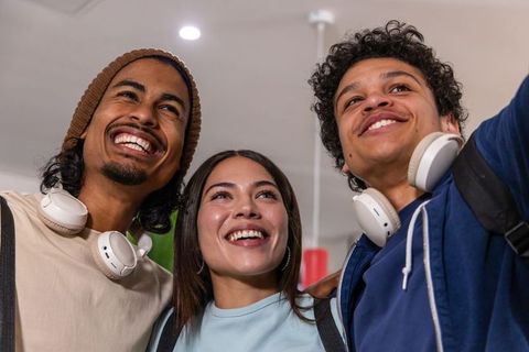 Multicultural young adults smiling and taking selfie in modern lobby wearing headphones