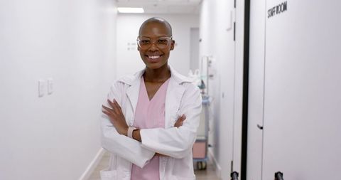 Smiling female doctor standing in clinic corridor wearing white lab coat and pink scrubs