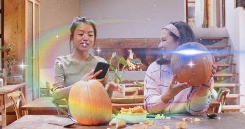 Mother daughter carving pumpkins by fireplace sharing cozy autumn family moment