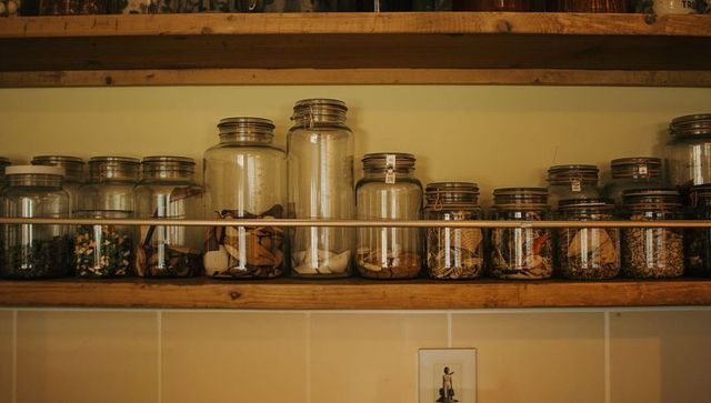 Rustic pantry shelf with assorted glass storage jars, metal guard rail and labeled lids
