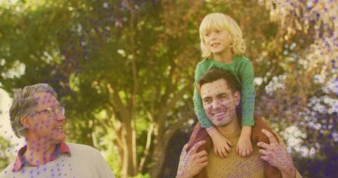 Multigenerational family walking in park, father carrying son on shoulders, smiling