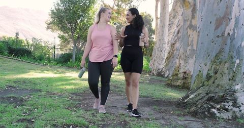 Two Friends Enjoying Nature Walk in Athletic Apparel with Bottles