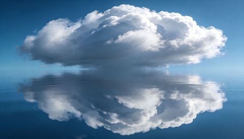 Single cumulus cloud reflecting on mirror-calm ocean surface with symmetric horizon
