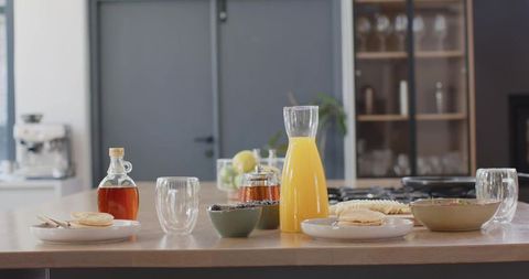 Sunlit breakfast spread on wooden kitchen island with orange juice, pancakes, fresh fruit