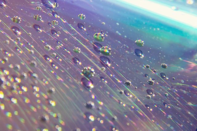 Colorful close-up focusing on water droplets dispersed on an iridescent surface, creating an abstract, reflective pattern. Ideal for backgrounds, design projects, educational materials on optics, or decorative purposes in media.