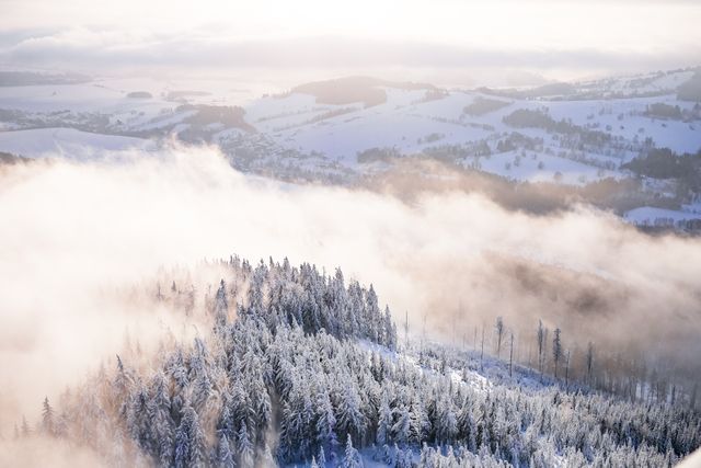 Winter scene shows an aerial perspective of snow-covered mountains and forests. Ideal for articles related to winter tourism, outdoor adventure, nature photography, environmental studies, or seasonal promotions.