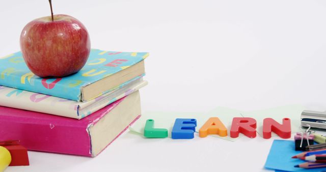 A stack of colorful books with a red apple on top and the word LEARN spelled out in letter magnets, with copy space. It represents a classroom setting, emphasizing education and the joy of learning.