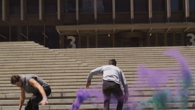 Dynamic and vibrant, this scene captures two individuals practicing parkour on urban steps, enhanced by colorful smoke trails. Useful for themes of adventure, sports, energy, metropolitan creativity, or urban life in promotional materials focusing on youth and movement. Ideal for websites, urban cultural projects, or advertisements related to sportswear or urban activities.