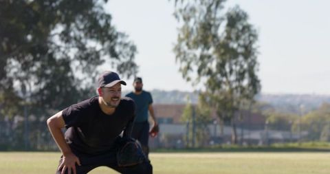 Crouching and standing baseball players practicing in sunlit park with glove and cap