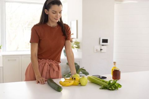 Woman standing at white kitchen island examining fresh produce and planning healthy meal