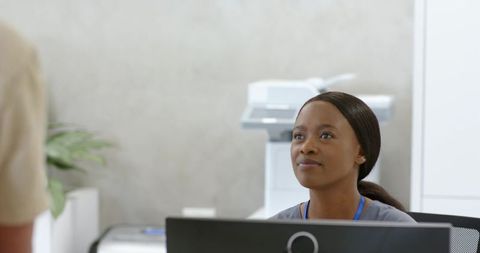 African american receptionist greeting visitor at clinic front desk, working with computer