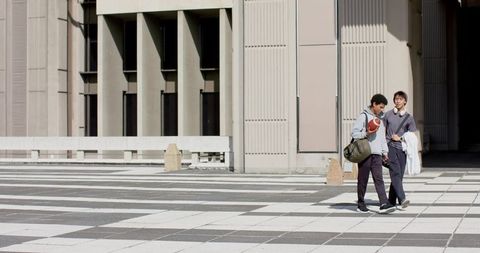 Multiracial friends walking across sunlit campus plaza carrying football and duffel bag