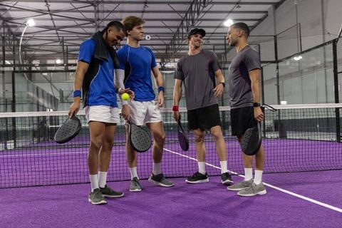 Four-player pickleball team sharing laughs on indoor purple court during friendly match