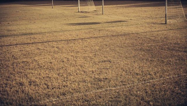 Empty soccer field at sunset with weathered turf, painted boundary lines, metal goals