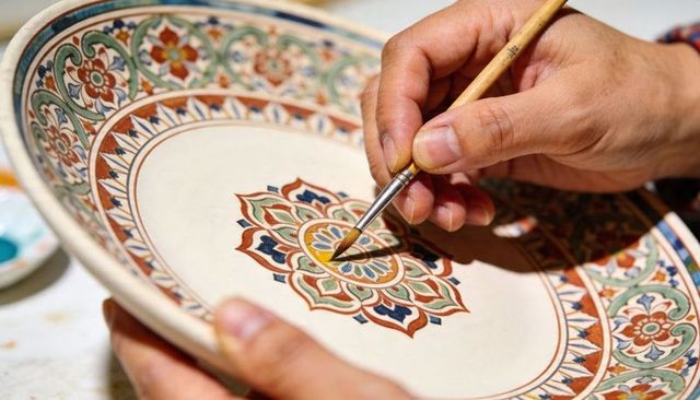 Artisan hand painting ceramic mandala plate with intricate floral and geometric patterns