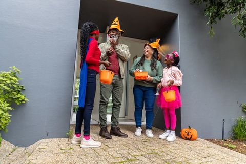 African american family celebrating halloween on porch sharing candy with costumed kids