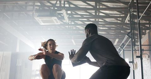 Focused athlete with trainer performing intense jump-squat in modern gym