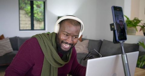 African American man laughing while livestreaming from home office with headphones and laptop