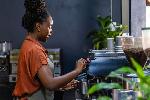 African american barista steaming milk at espresso machine in modern specialty cafe